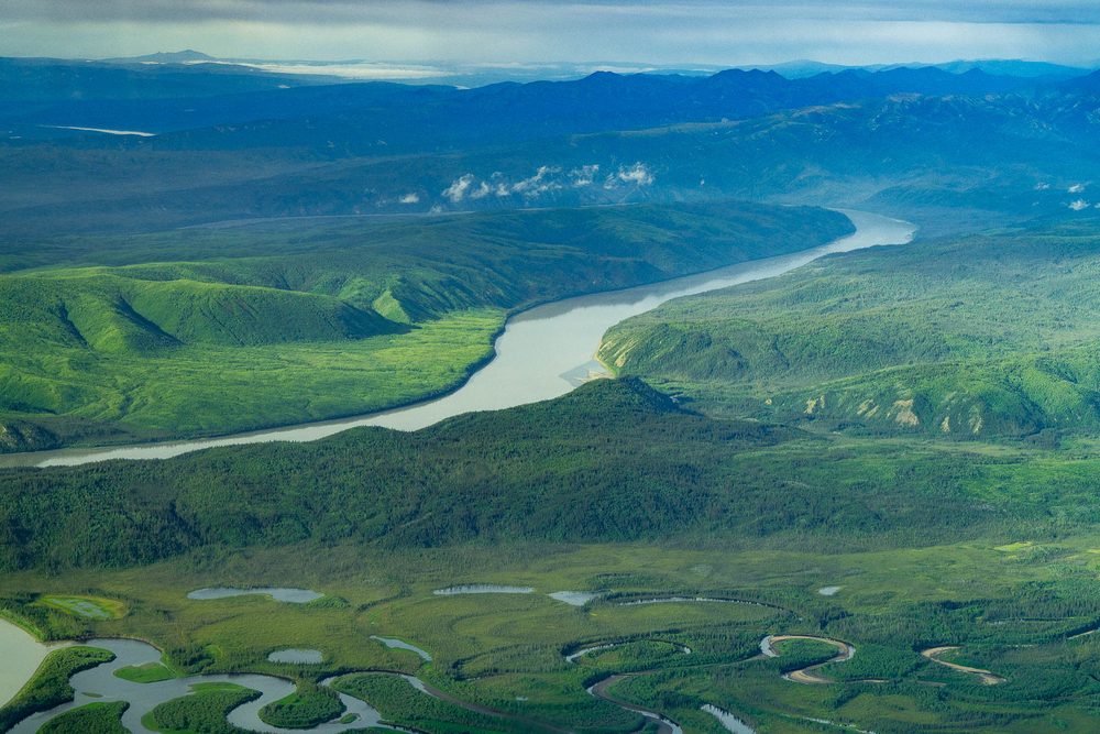 Aerial of a large river cutting through green hills under haze