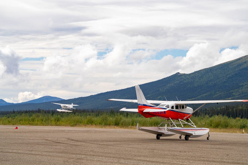 Small bush planes parked on a gravel airstrip below mountains