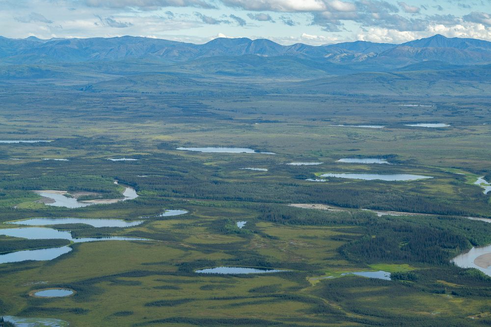Aerial of a lowland plain scattered with lakes below distant mountains