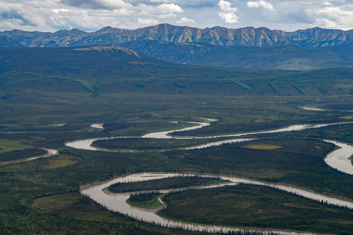 Aerial of a river looping across a wide valley floor below a long mountain range