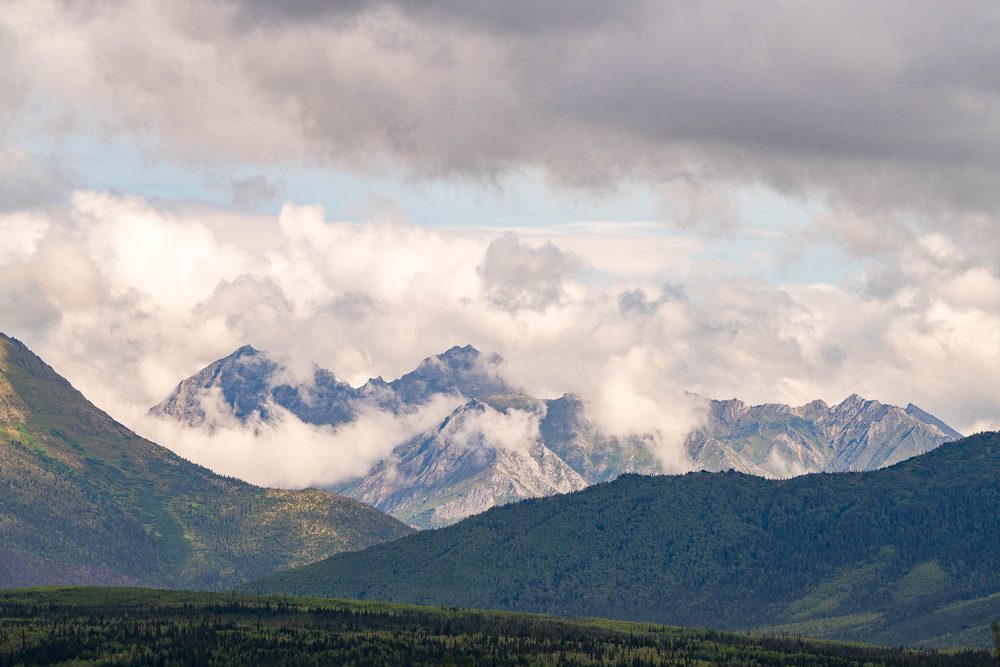 Jagged peaks half hidden in cloud beyond a green valley in the Brooks Range