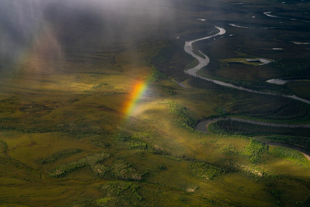 A rainbow falling onto tundra beside a winding river, seen from the air