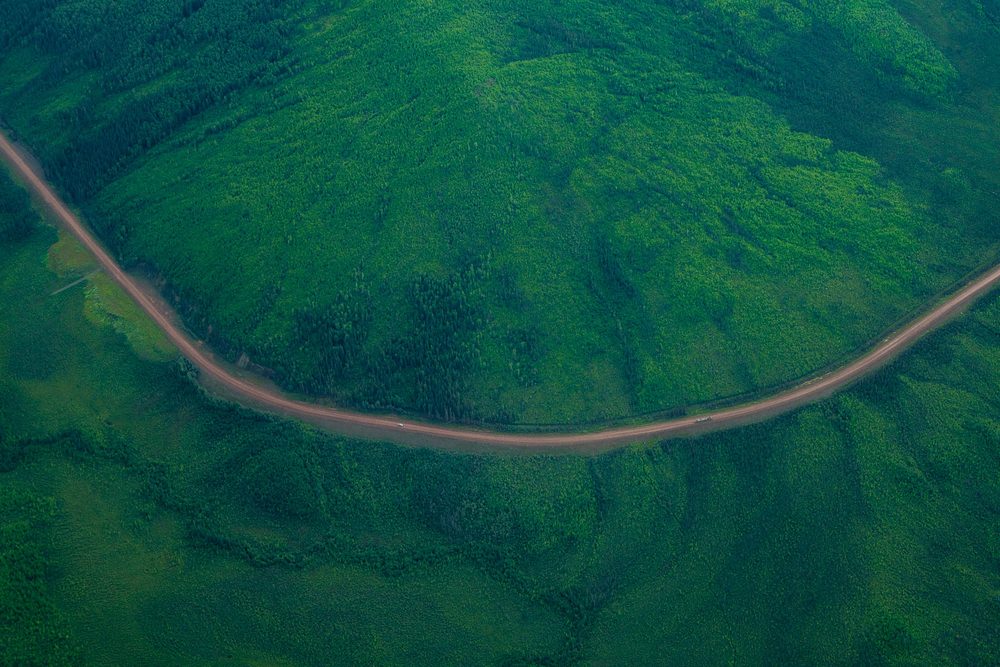Aerial looking down on a gravel road curving across a green hillside