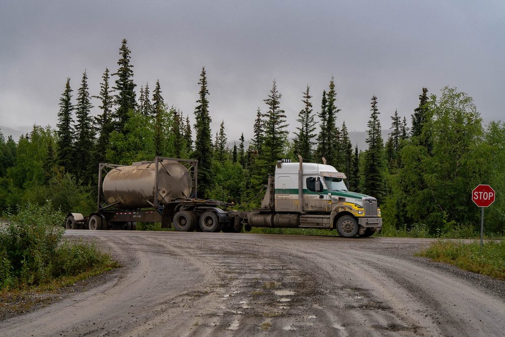 A tanker truck pulling onto a gravel haul road at a stop sign in the Alaskan interior