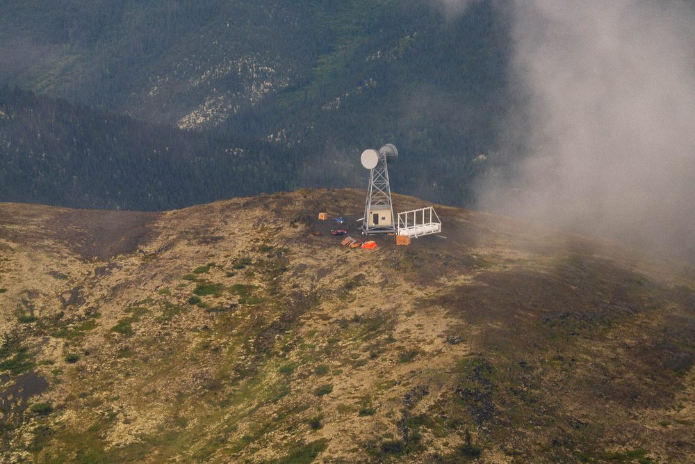 A communications tower and small structures on a ridgetop in cloud, from the air