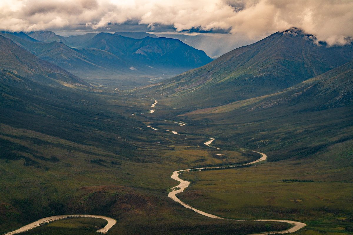 Aerial looking down a mountain valley as a river winds toward storm cloud in the Brooks Range