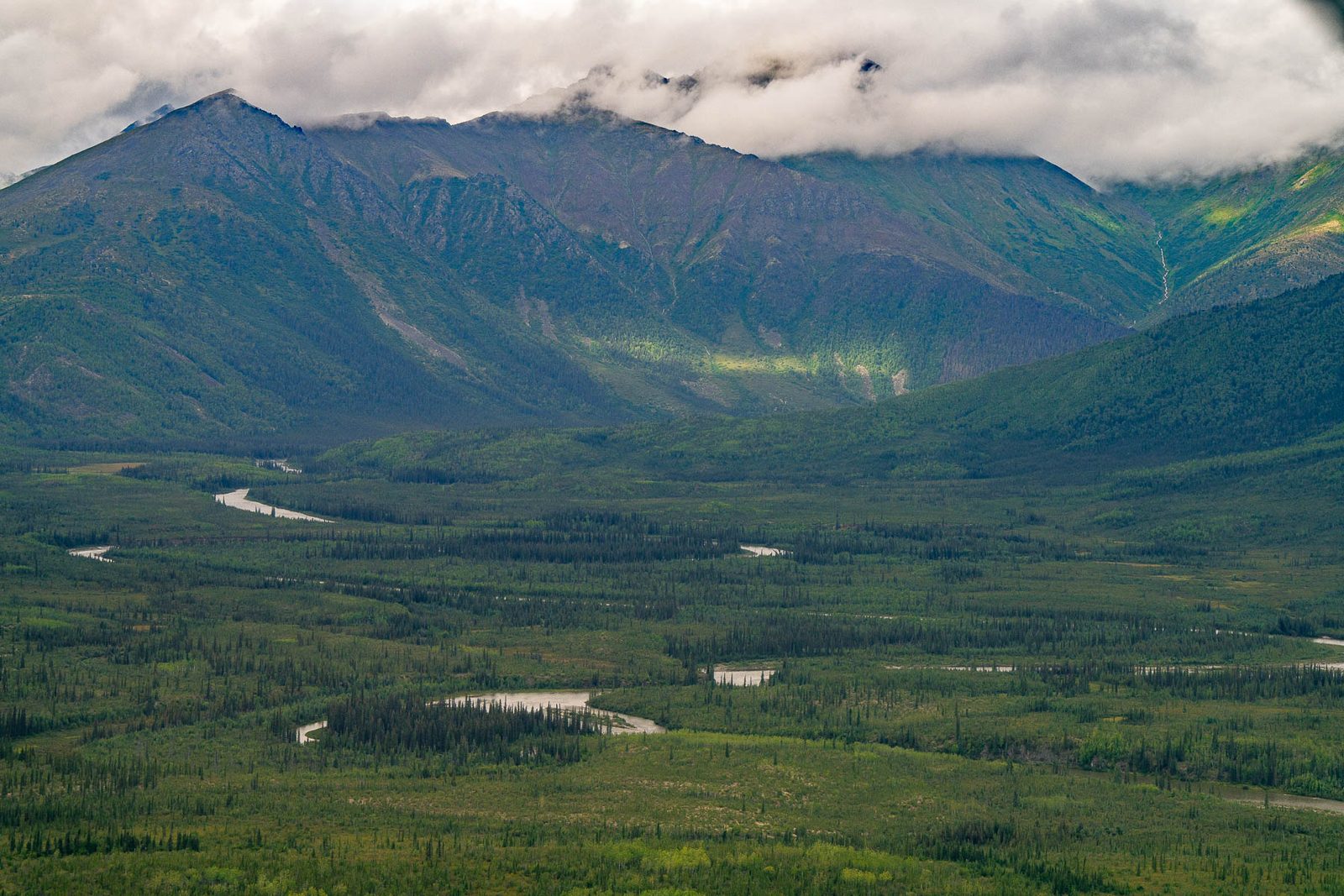 A broad valley below a long ridge with cloud lying along the summits