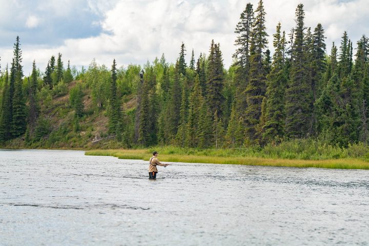 An angler casting from the shallows of a mountain lake
