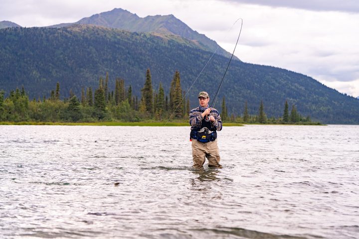 An angler mid-cast on a lake below the range