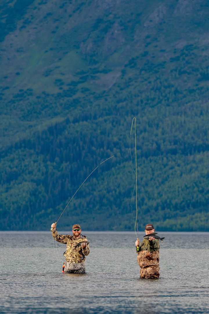 Two anglers in the water below a mountainside