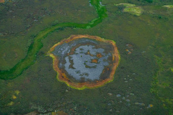 A tundra pond ringed in rust orange where iron stains the waterline