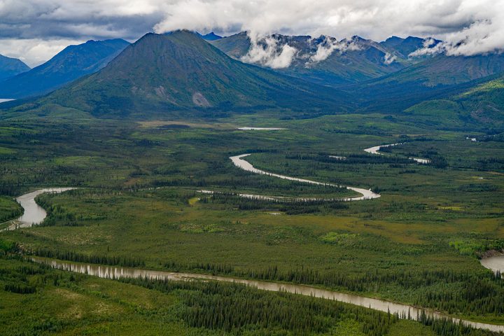A river meandering across a broad valley below a cloud-capped peak