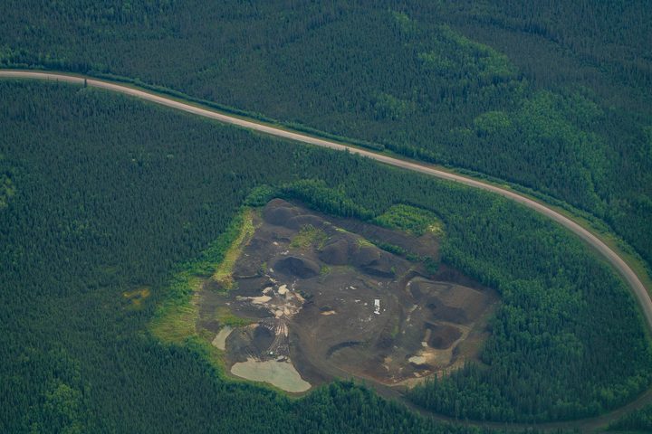 A gravel road curving past a stripped material site cut into the forest