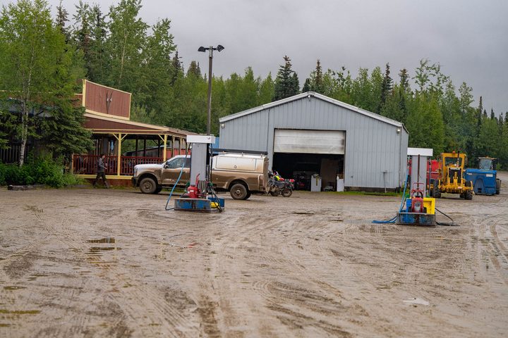Fuel pumps and a steel garage in the mud yard of a roadhouse on the haul road