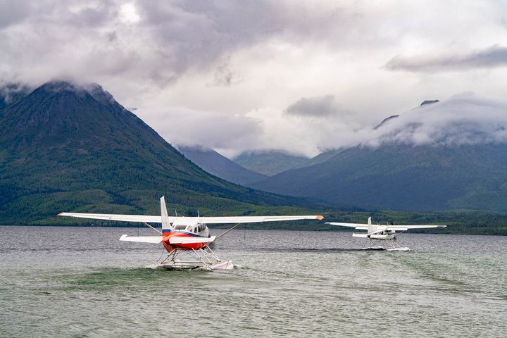 Two floatplanes on a lake below cloud-covered mountains