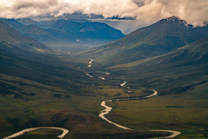 A river winds down a mountain valley toward storm cloud