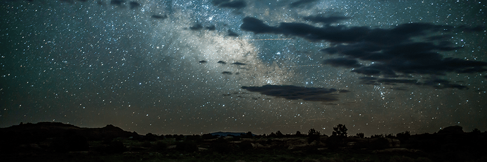 Clouds sail across a star-filled sky above The Needles | Canyonlands National Park Facts