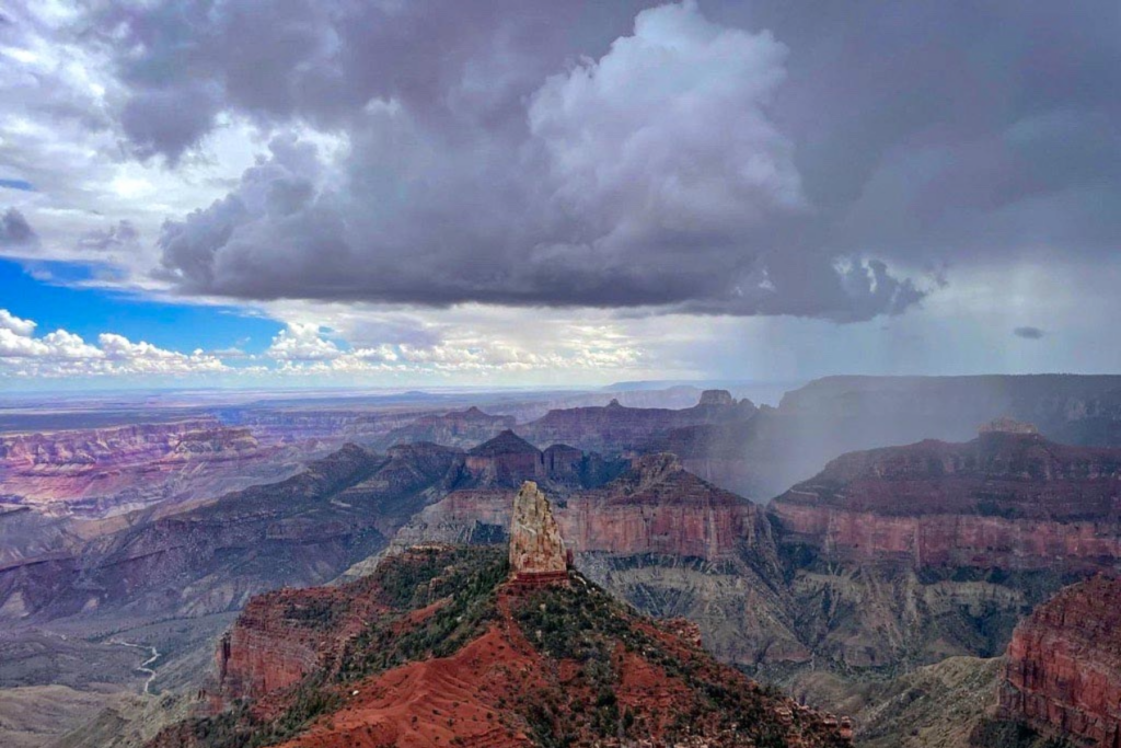 Grand Canyon National Park's North Rim as a monsoon storm rolls in with rain on the right and blue skies on the left.