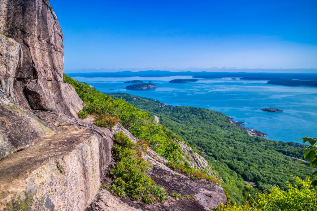 A cliffside view of the Precipice Trail in Acadia National Park with greenery at the base connecting to vast views of the ocean and islands.
