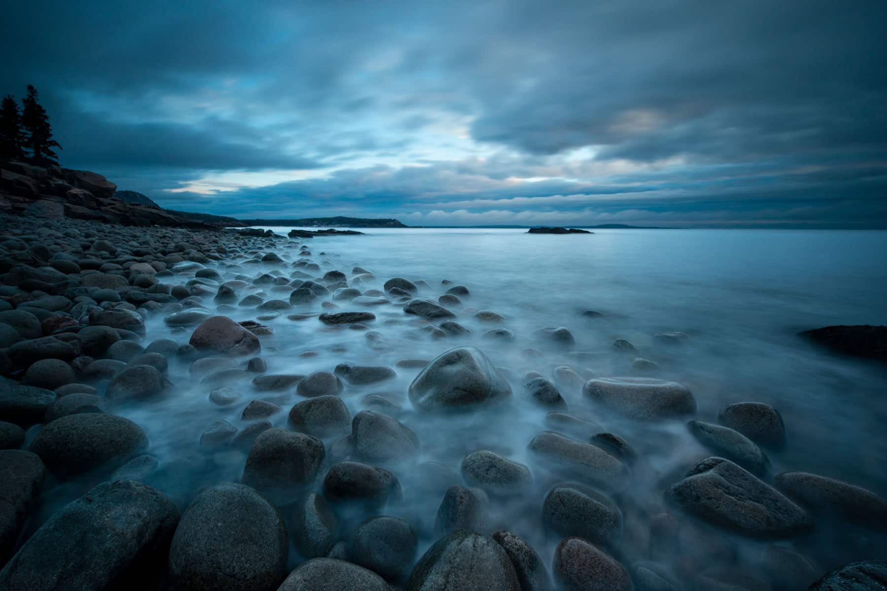 Stormy skies over a boulder filled beach in Acadia National Park in winter.