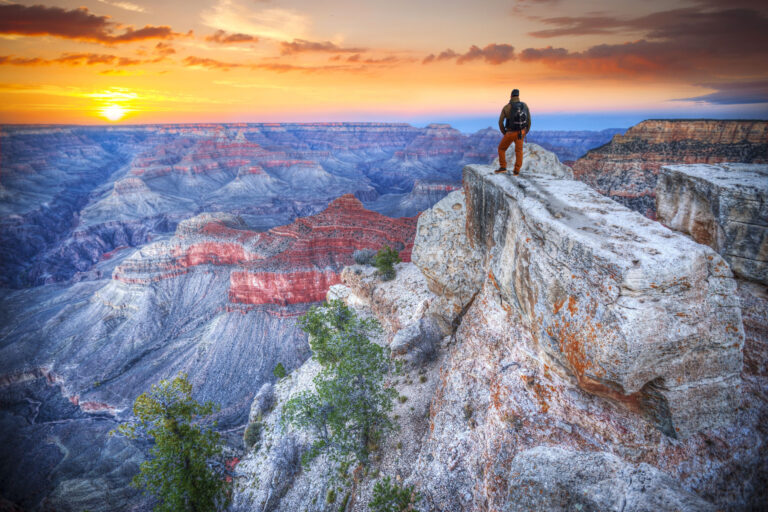 A man standing on a cliff over the Grand Canyon at sunrise.