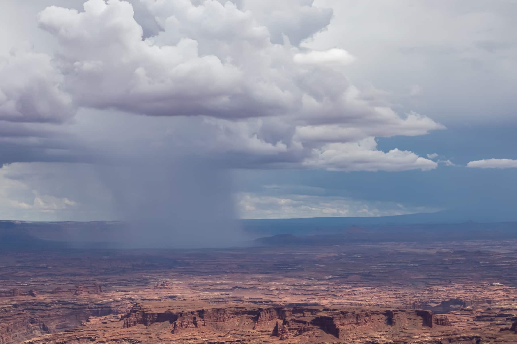 A rain shaft falls from clouds at the Grand View Point of Canyonlands National Park. 