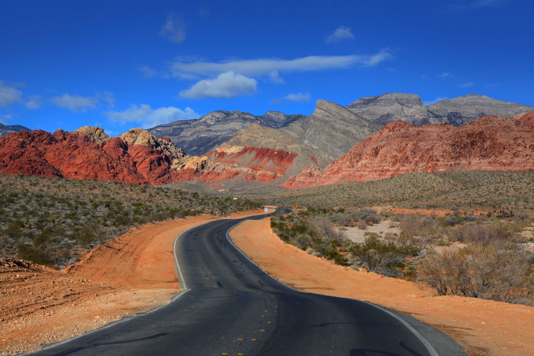 A black road leads to colorful sandstone cliffs in the distance at Red Rock Canyon near Las Vegas. 