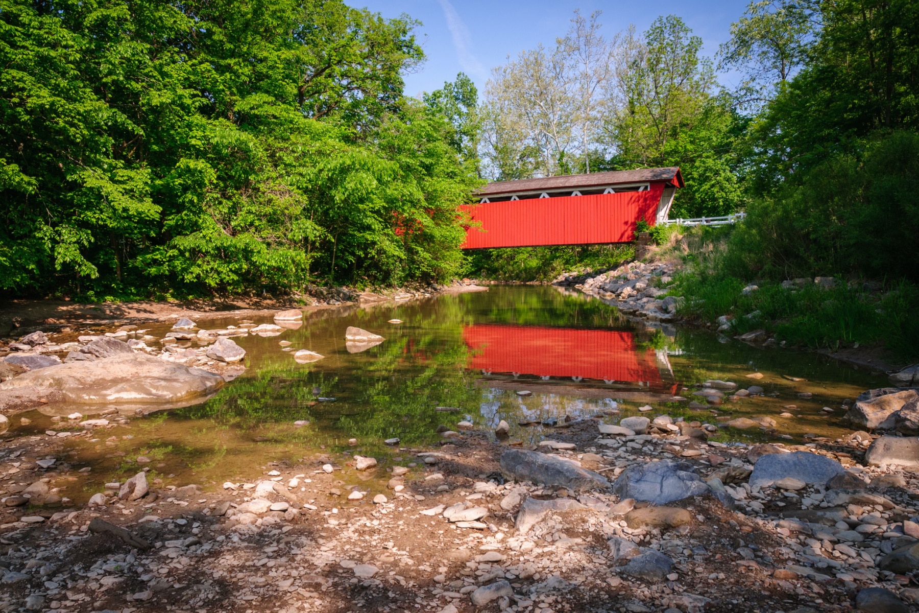 A red covered bridge over a river filled with rocks and trees on each side in Cuyahoga Valley National Park.
