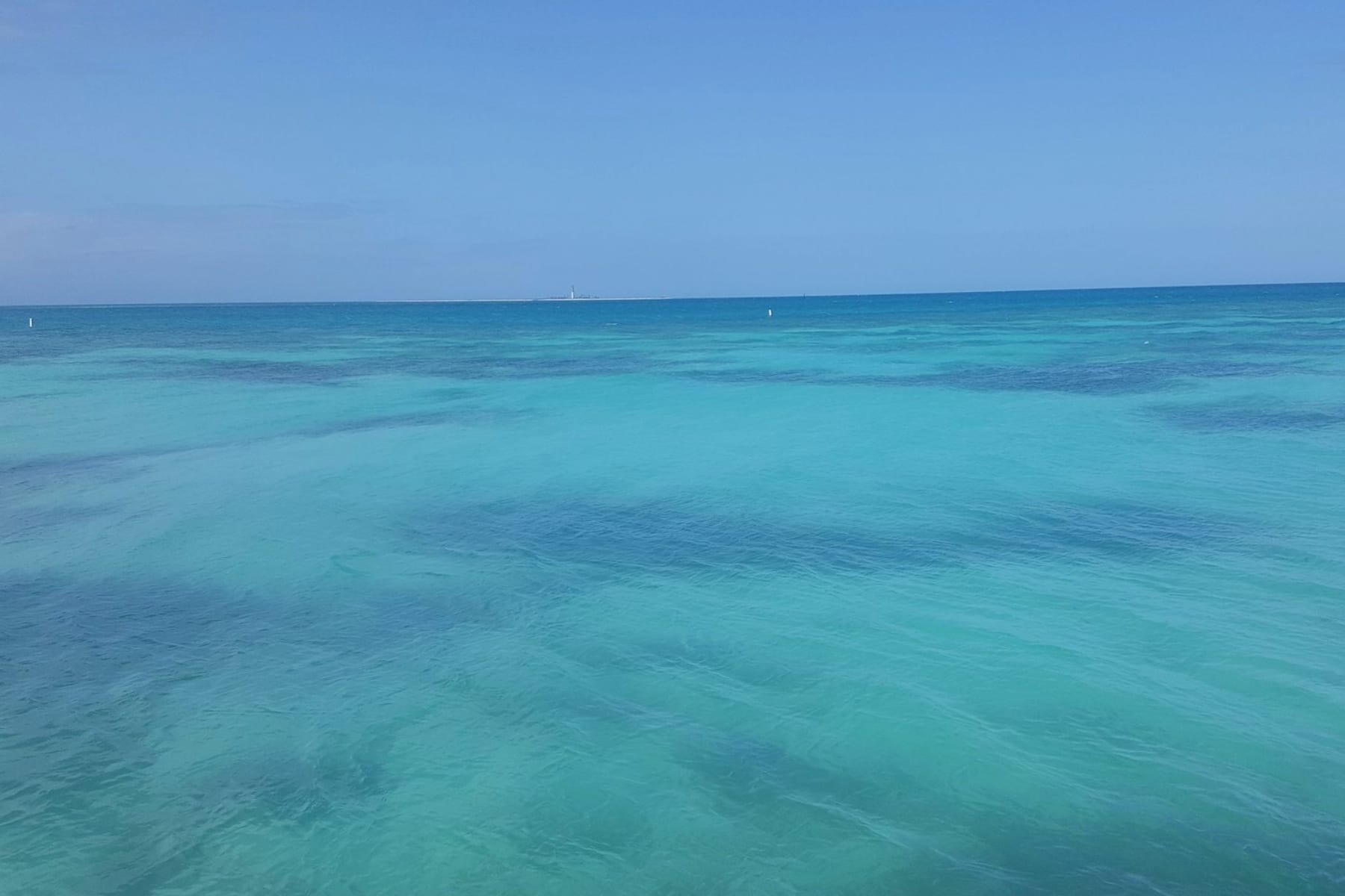 Turquoise water of Dry Tortugas National Park with a lighthouse in the far distance.