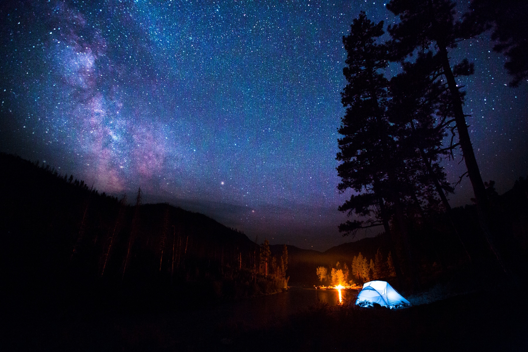 An illuminated tent and campfire under starry skies.