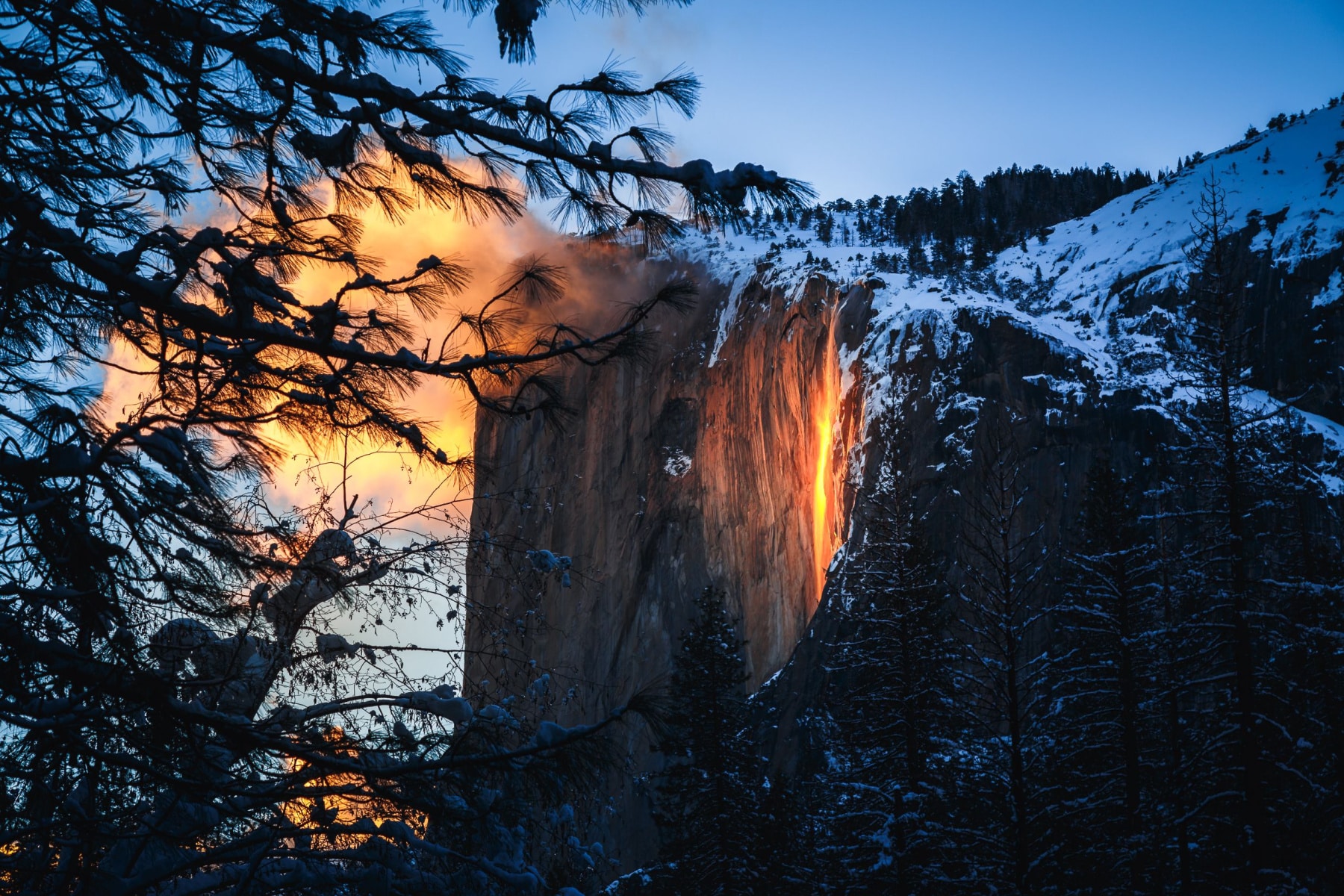 Yosemite Firefall seen from a distance with fog also glowing orange.