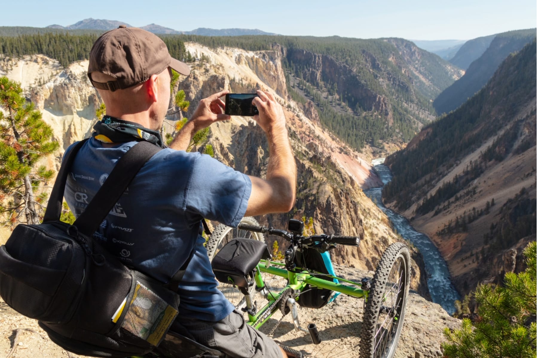 A man taking a photo with an off-road wheelchair nearby and the Grand Canyon of the Yellowstone in front of him. 