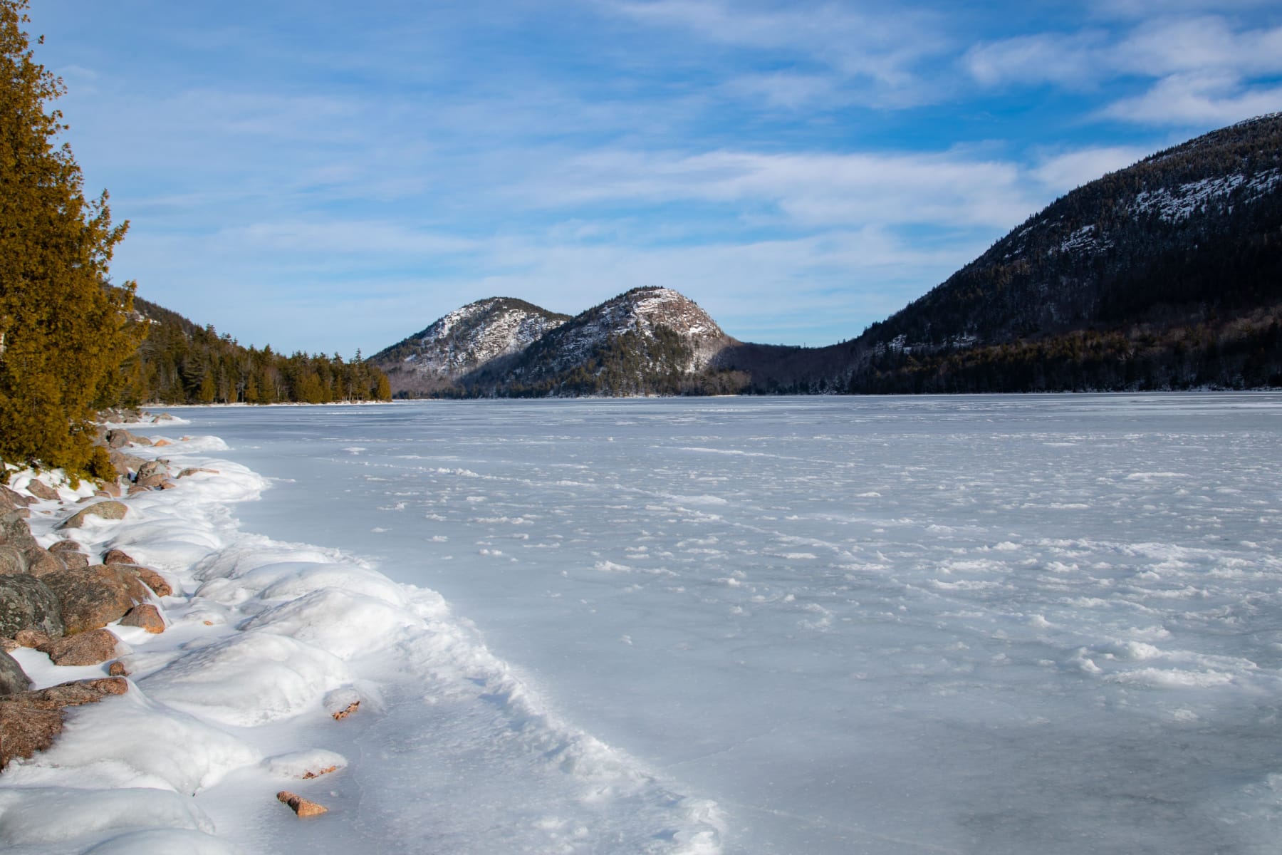 Jordan Pond in Acadia frozen in the winter with mountains in the distance. 