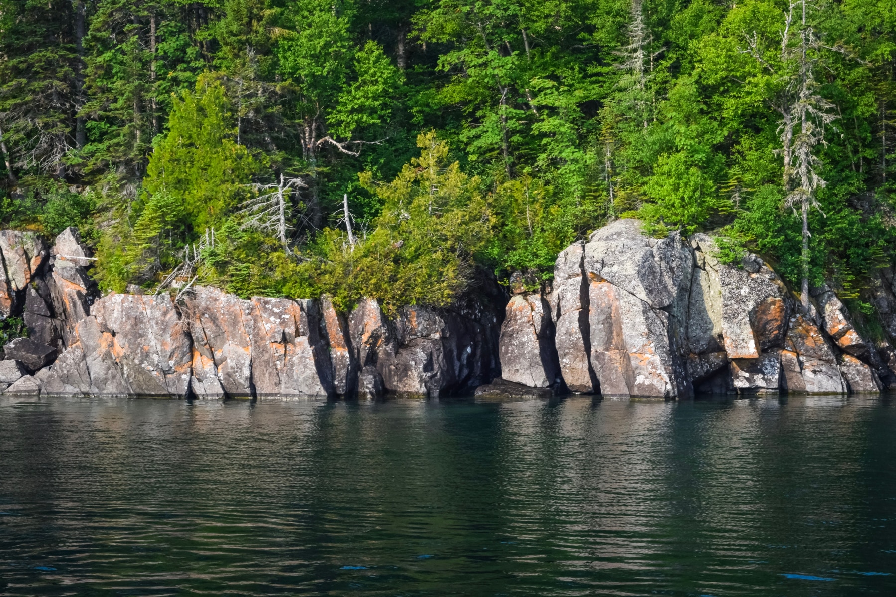 Rocky cliffs adorned with trees stand over Lake Superior.