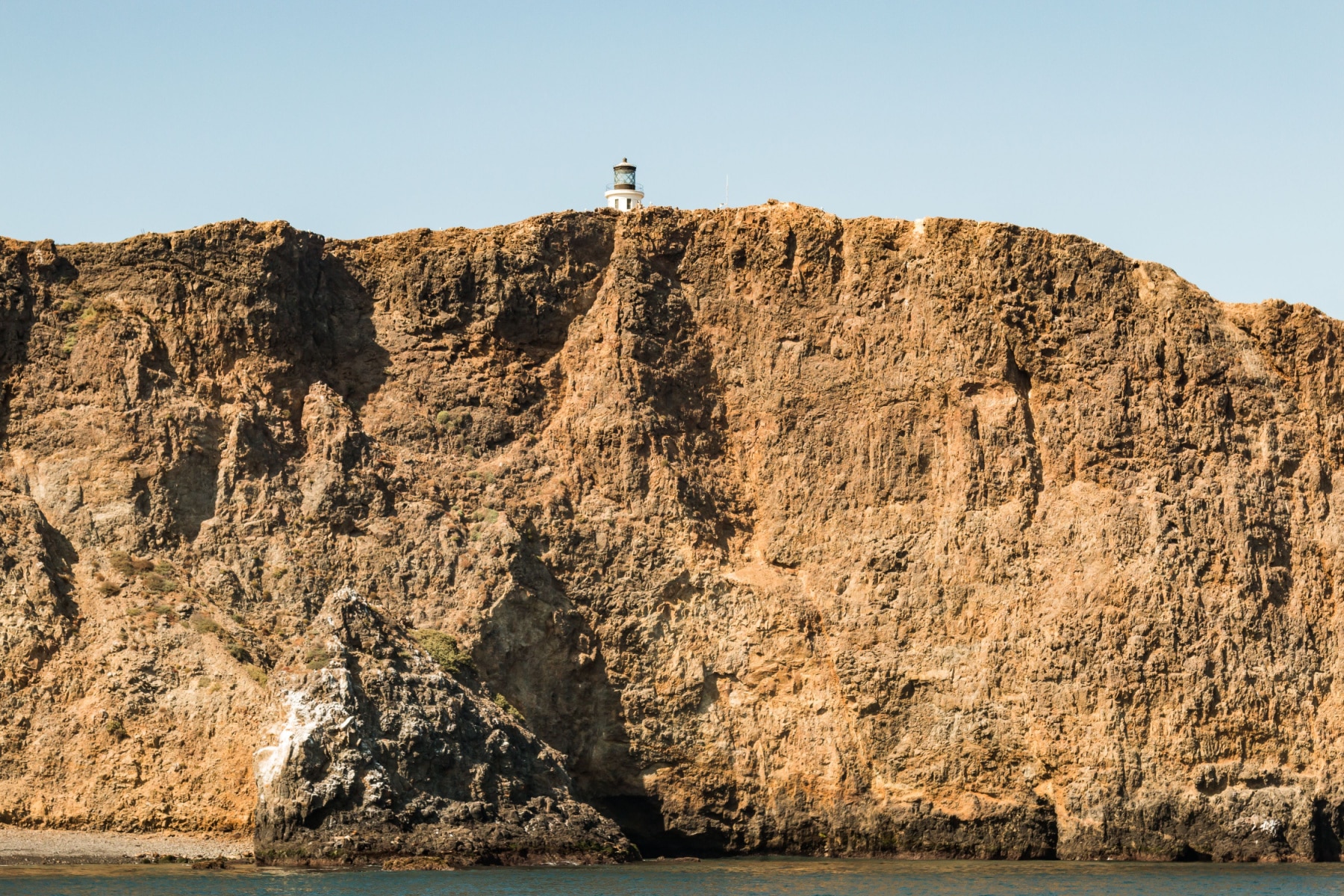 Tall cliffs rise above the water with Anacapa Island Light Station peeking out above. 