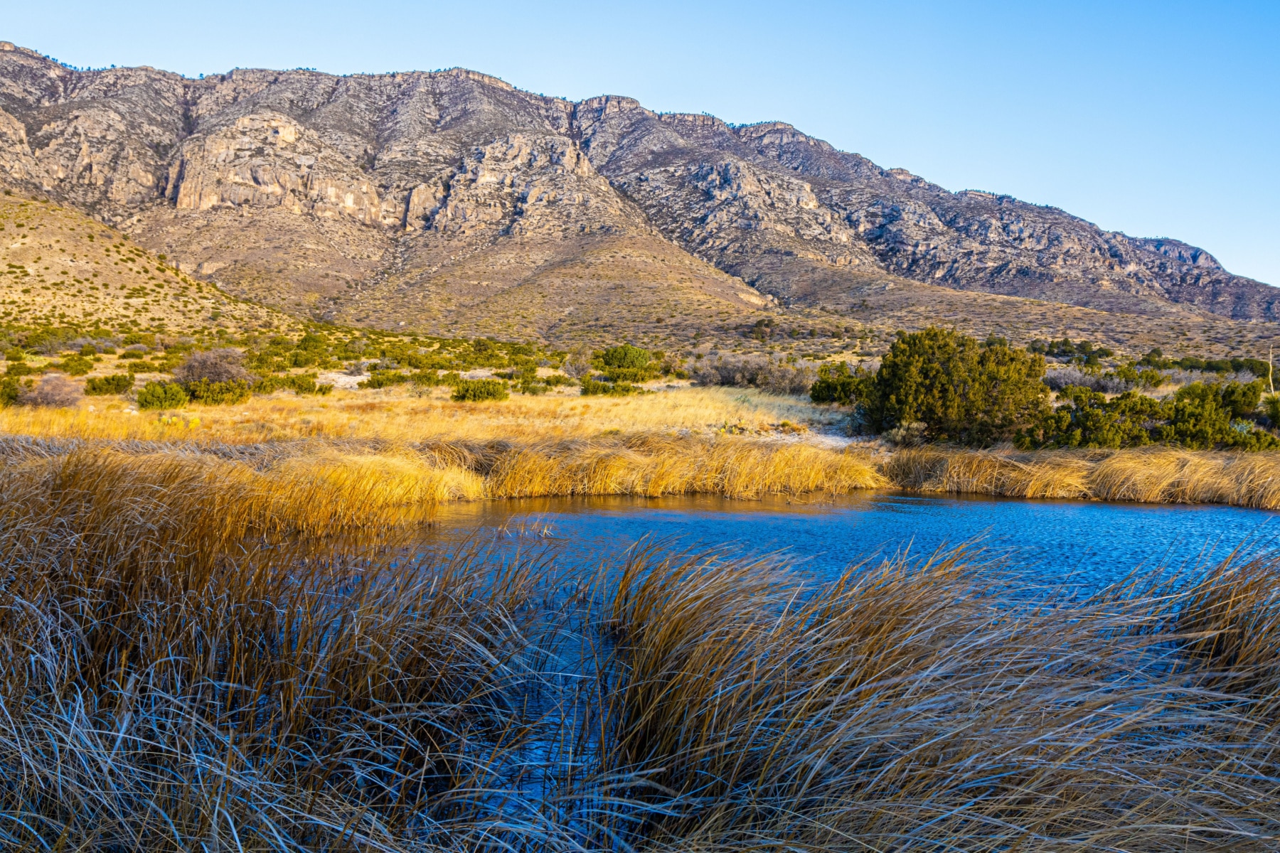 A lake sits in front of the Guadalupe Mountain Range, towering above.