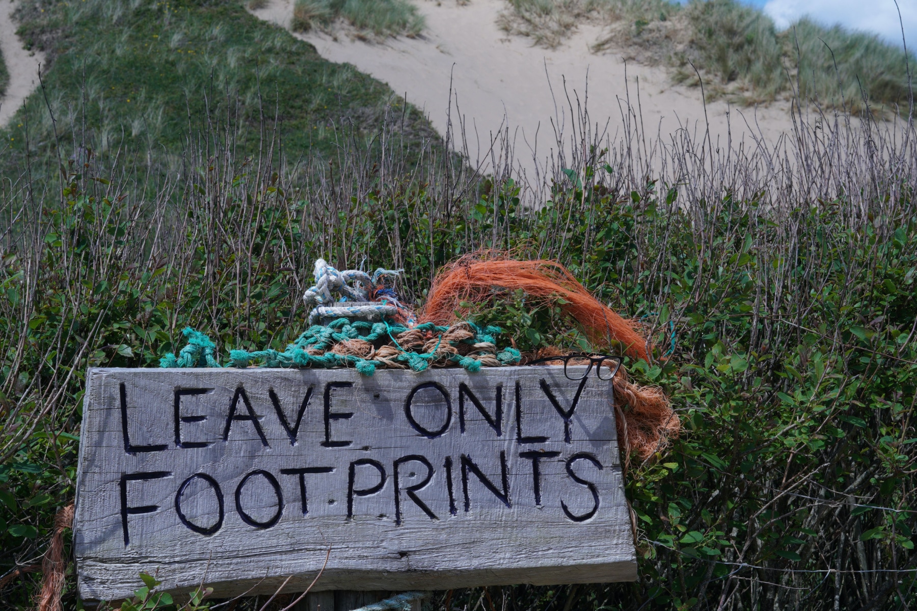 Sign reads "Leave Only Footprints" on a path leading to a beach, part of adapting the 7 principles of leave no trace. 
