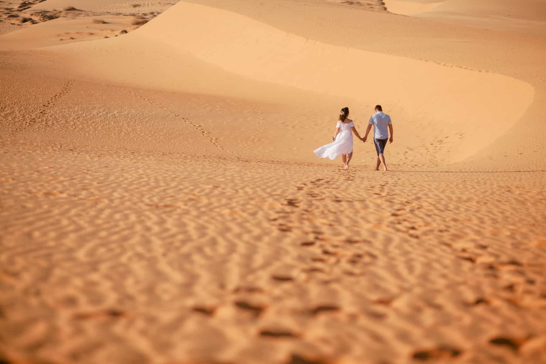 Married couple walking across sand dunes.
